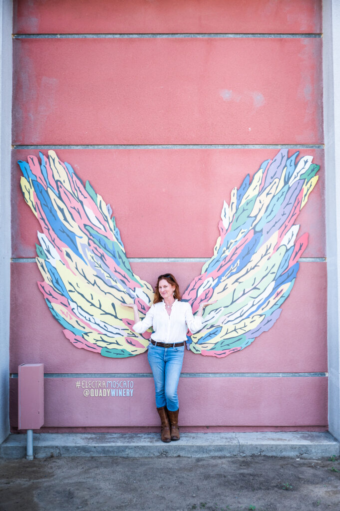 Alison Needham standing in front of the wings mural at Quady Winery