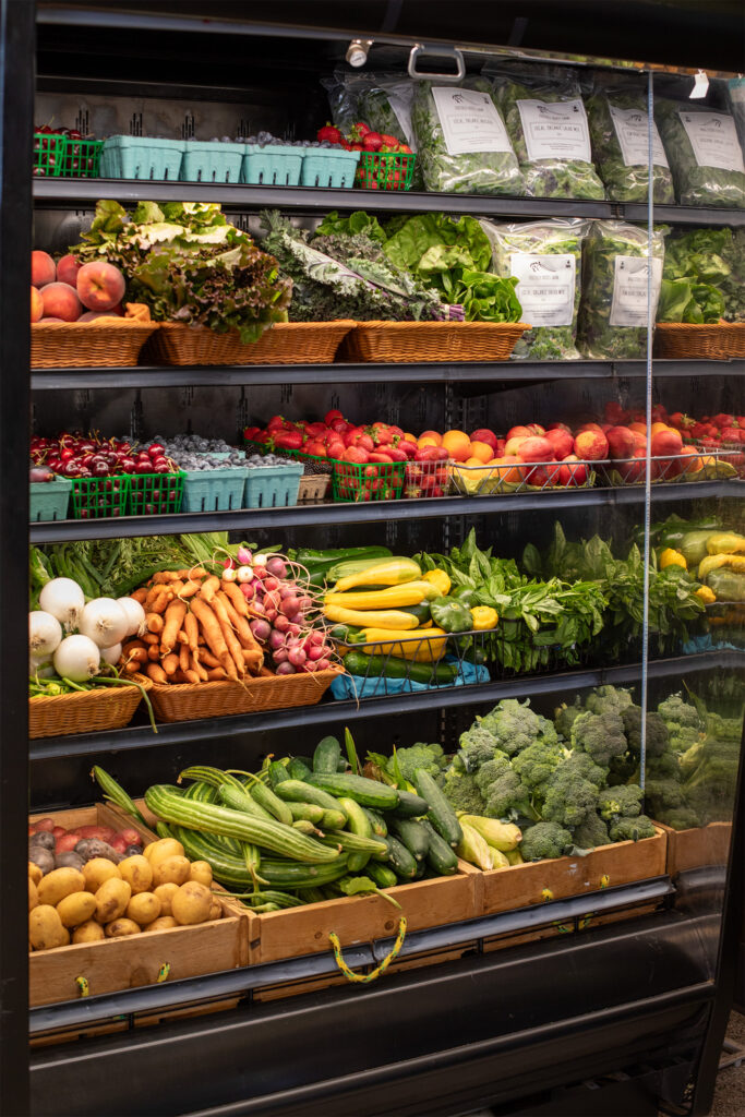 Cooler filled with various produce like carrots, summer squash, cucumbers, broccoli, and stone fruit