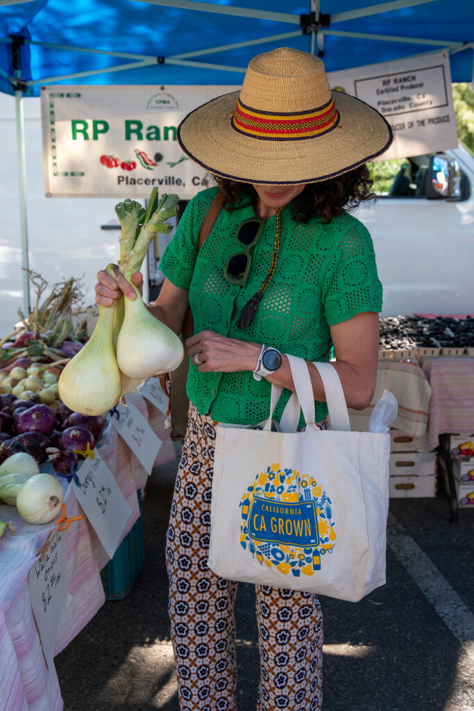 Person holding onions and California grown tote at farm stand