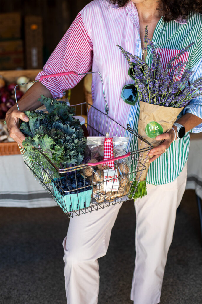 Person holding wire basket with kale, nuts, berries, and a flower bouquet